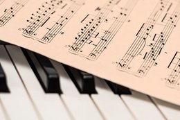 Ein Blatt mit Noten liegt schräg auf einer Klaviertastatur.