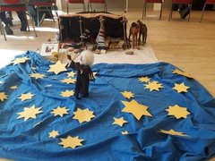 Auf einer blauen Decke liegen gelbe Sterne. In der Mitte steht eine Stofffigur, gekleidet in einen schwarzen Mantel mit weißem, wallenden Haaren.